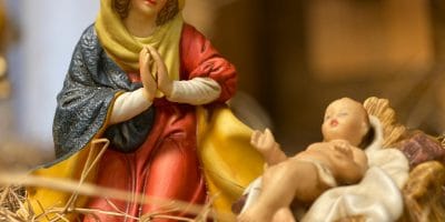 Close-up of nativity figurines featuring Virgin Mary and baby Jesus on a straw bed symbolizing Christmas.