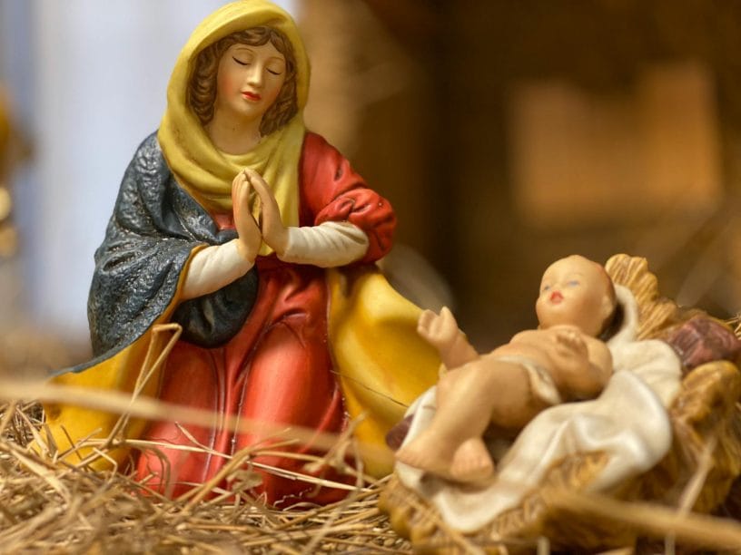 Close-up of nativity figurines featuring Virgin Mary and baby Jesus on a straw bed symbolizing Christmas.