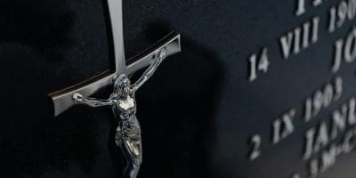 Detailed photo of a cross on a tombstone featuring engraved text, representing religious themes.