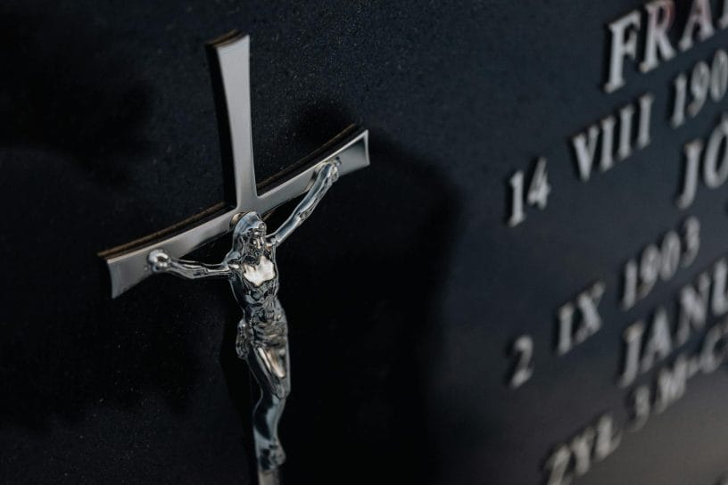 Detailed photo of a cross on a tombstone featuring engraved text, representing religious themes.