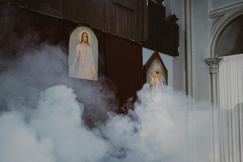An atmospheric church interior featuring holy paintings shrouded in mist.